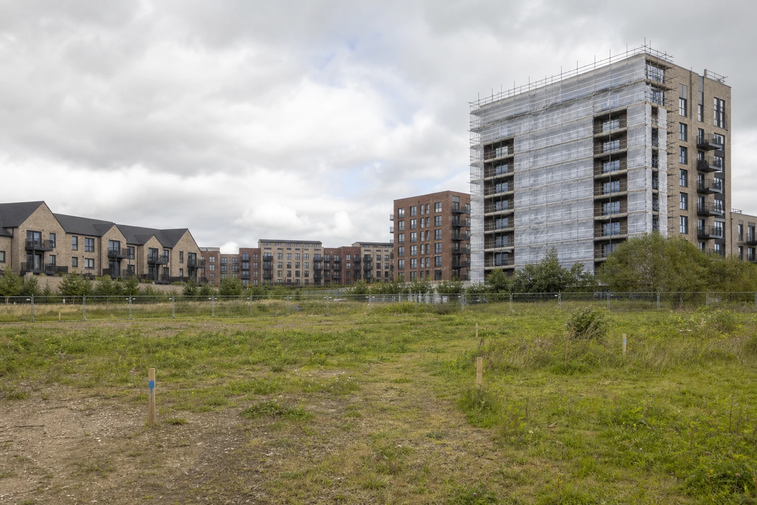 Undeveloped UK housing land beside apartment blocks undergoing cladding remediation